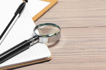 Magnifying glass and notebook on wooden table