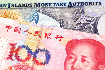 A Chinese, red one hundred yuan renminbi bank note close up in macro with colorful money from the Cayman Islands