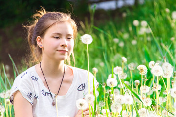 Cute girl among dandelions on a green meadow.
