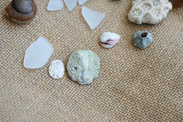 Fototapeta na wymiar Sea glasses, shells and stones on a rough woven background close-up. Vacation concept