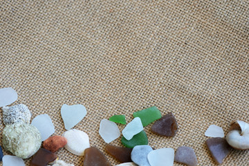 Fototapeta na wymiar Sea glasses, shells and stones on a rough woven background close-up. Vacation concept
