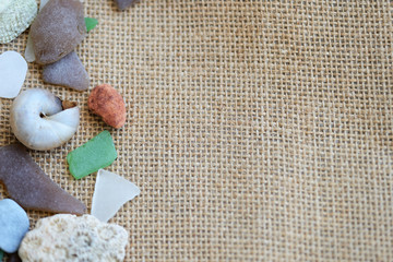 Sea glasses, shells and stones on a rough woven background close-up. Vacation concept
