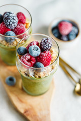 Top view on portions of chia pudding with matcha tea, organic granola, frozen berries in glasses. The concept of healthy vegan food.