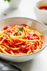 Traditional pasta with tomato and Greek basil sauce in a ceramic bowl on a white table.