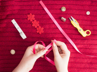 Woman ties a pink ribbon bow on red wool fabric dress