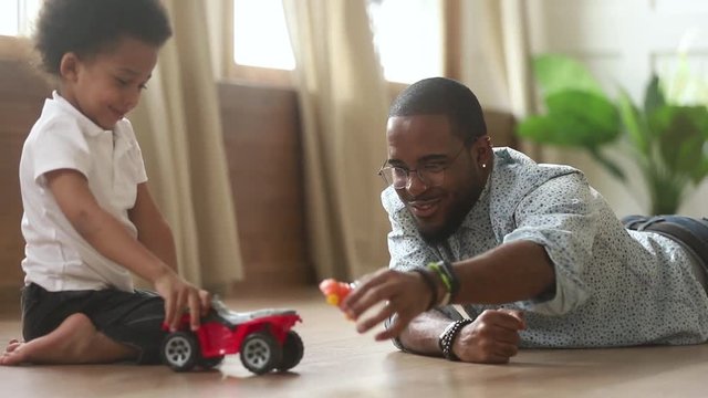 Happy african cute little son playing toy cars with dad