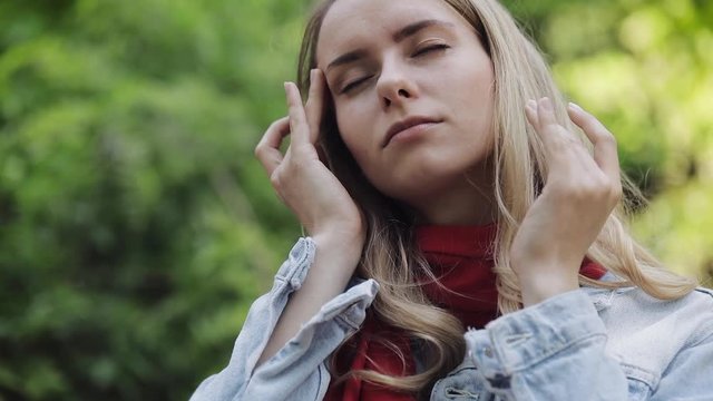 Young woman wearing red scarf with headache standing in the park. Girl feel ill unhappy and with migraine touching her temples. Dreadful migraine.