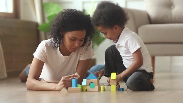 African mom helping kid son building castle from wooden blocks