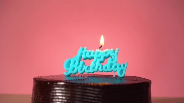 Chocolate cake on red background with lighting blue happy birthday candle and confetti falling down making wish blowing out candle 
