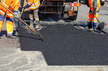 The working team smoothes hot asphalt with shovels by hand when repairing the road.