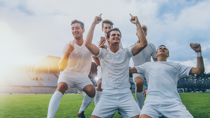 Fototapeta Captain of the Soccer Team Stands on His Knees Celebrates Awesome Victory, Makes YES Gesture Champion Team Joins Him. Successful Happy Football Players Celebrate Victory. Shot with Warm Sunlight Flare obraz