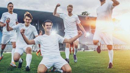 Captain of the Soccer Team Stands on His Knees Celebrates Awesome Victory, Makes YES Gesture Champion Team Joins Him. Successful Happy Football Players Celebrate Victory. Shot with Warm Sunlight Flare