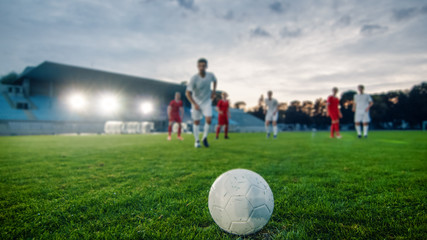Shot of a Football Ball Lying on a Stadium Grass. Professional Soccer Player Outruns Members of Opposing Team and Ready to Kick the Ball to Score Goal.