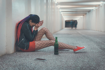 Woman crying after phone call. A young girl in depression drinks whiskey. Homeless girl sitting in despair in the underpass. Emotional experience