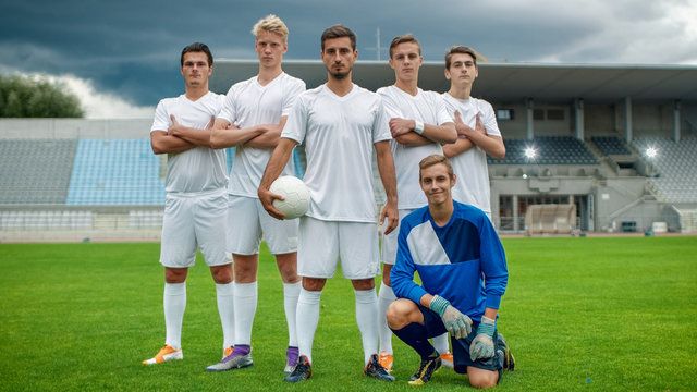 Professional Soccer Players Team Posing for a Group Photo Standing on a Football Field, Goalkeeper Sitting and Smiling.
