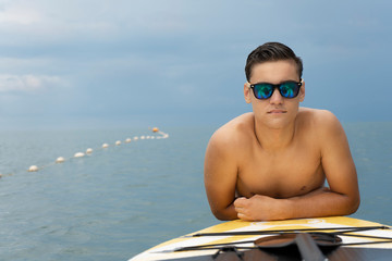 Surfer in sunglasses posing with surfboard on the beach. Active lifestyle and summer vacations. Copy space