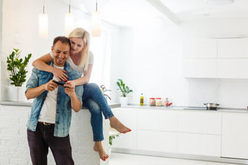 couple, woman and man using smartphone at kitchen. Ultra wide home shot.