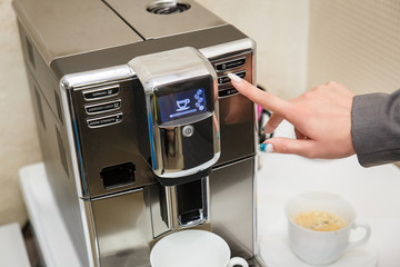 The girl chooses the mode of making coffee on the coffee machine. Female hand presses the button on the coffee machine .