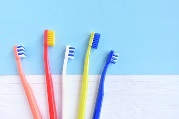 Colorful toothbrushes with selective focus on blurred blue background. Dental tools for daily teeth protection. Multicolored plastic toothbrush with bright bristles with soft focus. Oral hygiene 