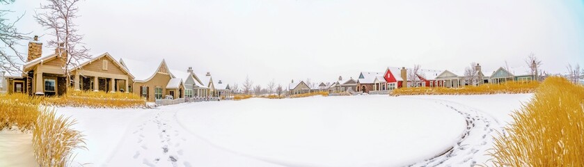 Scenic winter view of snow covered ground in front of houses under cloudy sky