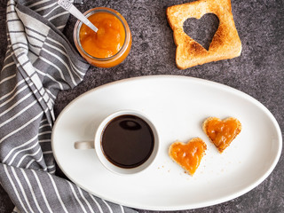 Kaffee und Toastbrot mit Aprikosenmarmelade in Herzform auf einem ovalen weißen Teller, Draufsicht, Frühstück