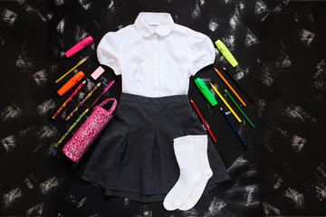 White shirt, grey skirt and stationery supplies on black background. The first of september, new school year.