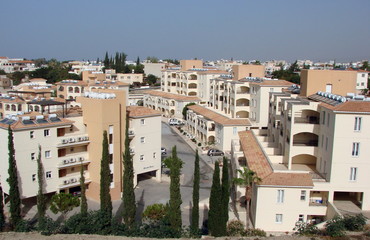 A top view of the snowy houses of residential areas of the city surrounded by lush green cypresses under the rays of a rising sun against the background of a blue sky.