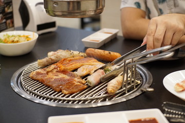 A man grilling porks ,hotdog, Glazed Pork and Vegetable on Charcoal grilled Korean-Style BBQ.