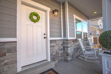 Facade of a home with a simple wreath hanging on the white wooden door © Jason