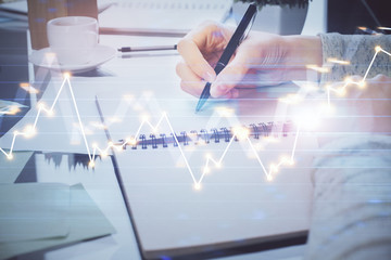 Hand taking notes in notepad. Forex chart holograms in front. Concept of research. Double exposure