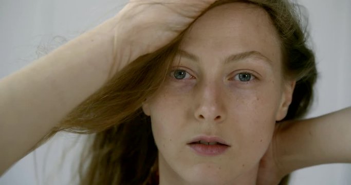 charming no makeup woman is looking at camera and playing with her long hair