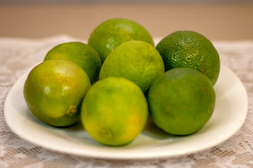 Green lemons served on white porcelain plate on a table covered with white lace towel.
