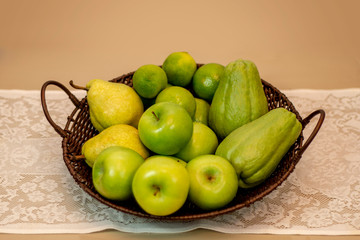  Fruits and vegetables of green color inside basket brown on white lace tablecloth.