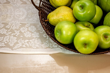  Fruits and vegetables of green color inside basket brown on white lace tablecloth.