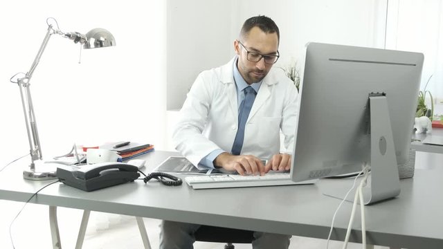 portrait of a handsome man male doctor in medical practice office working on computer