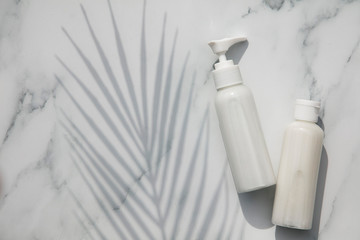 White cosmetics bottles on a marble background with a tropical leaf shadow