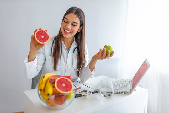 Doctor Or Nutritionist Hold An Apple. Good Medical Healthcare Nutrition Concept. An Apple A Day Keeps The Doctor Away. Smiling Female Nutritionist Holding A Green Apple And Showing Healthy Fruits