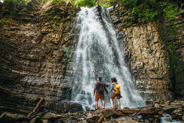 Man and woman hikers trekking a rocky path against the background of a waterfall and rocks. Hiker...