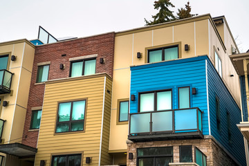 Residential building with horizontal siding concrete and brick on the wall. The building also features a flat roof and balconies with glass railing.