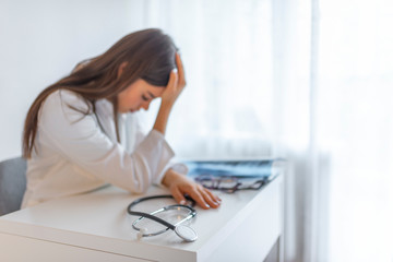 Stethoscope and doctor sitting with laptop stress headache about work in hospital. Frustration young female doctor sitting in her consulting room and looking at document.