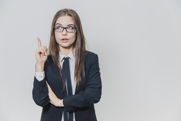 Young pretty businesswoman is pointing her finger up with an amusement, amazement and dazzling facial expression.