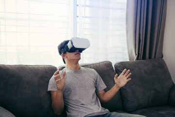 Young asian man wearing virtual reality glasses at living room for admiring virtual reality.