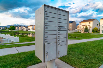 White metal cluster mailbox with pond grassy terrain and homes in the background