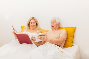 COUPLE SENIOR LISANT LIVRE ET TABLETTE DANS UN LIT