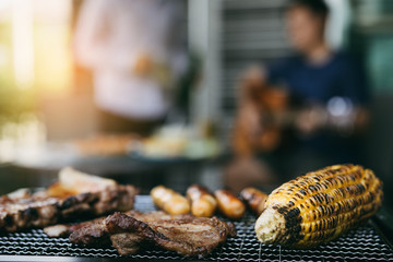 Close up grilled meats and various food on the grill and celebrations of friends who are playing...