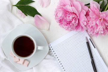 Cup of coffee with notepad. Morning coffee mug for breakfast, empty notebook and pink peony flowers in flatlay style. Breakfast blogger writer, blank white sheet for writing