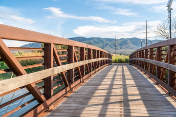 Fototapeta na wymiar Wooden bridge with metal lattice guardrail over a lake with view of mountain
