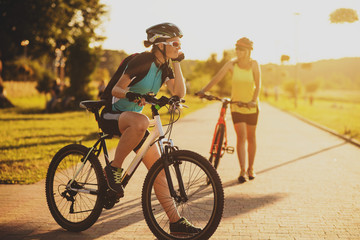 Two women friends riding on bikes at the sunset