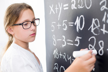 The girl in glasses writes with chalk on the school blackboard.