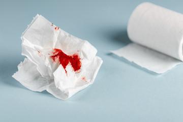 A photo of used bloody toilet paper and a toilet paper roll on the light blue background